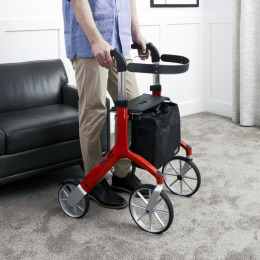 Four wheeled walker in use by a standing man in front of a sofa chair